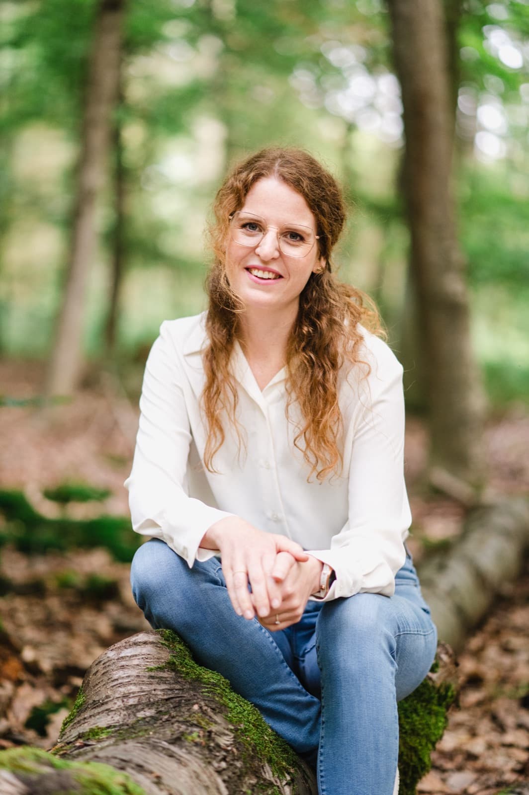 Lisa Engel sitzt lächelnd auf einem moosbewachsenen Baumstamm im Wald